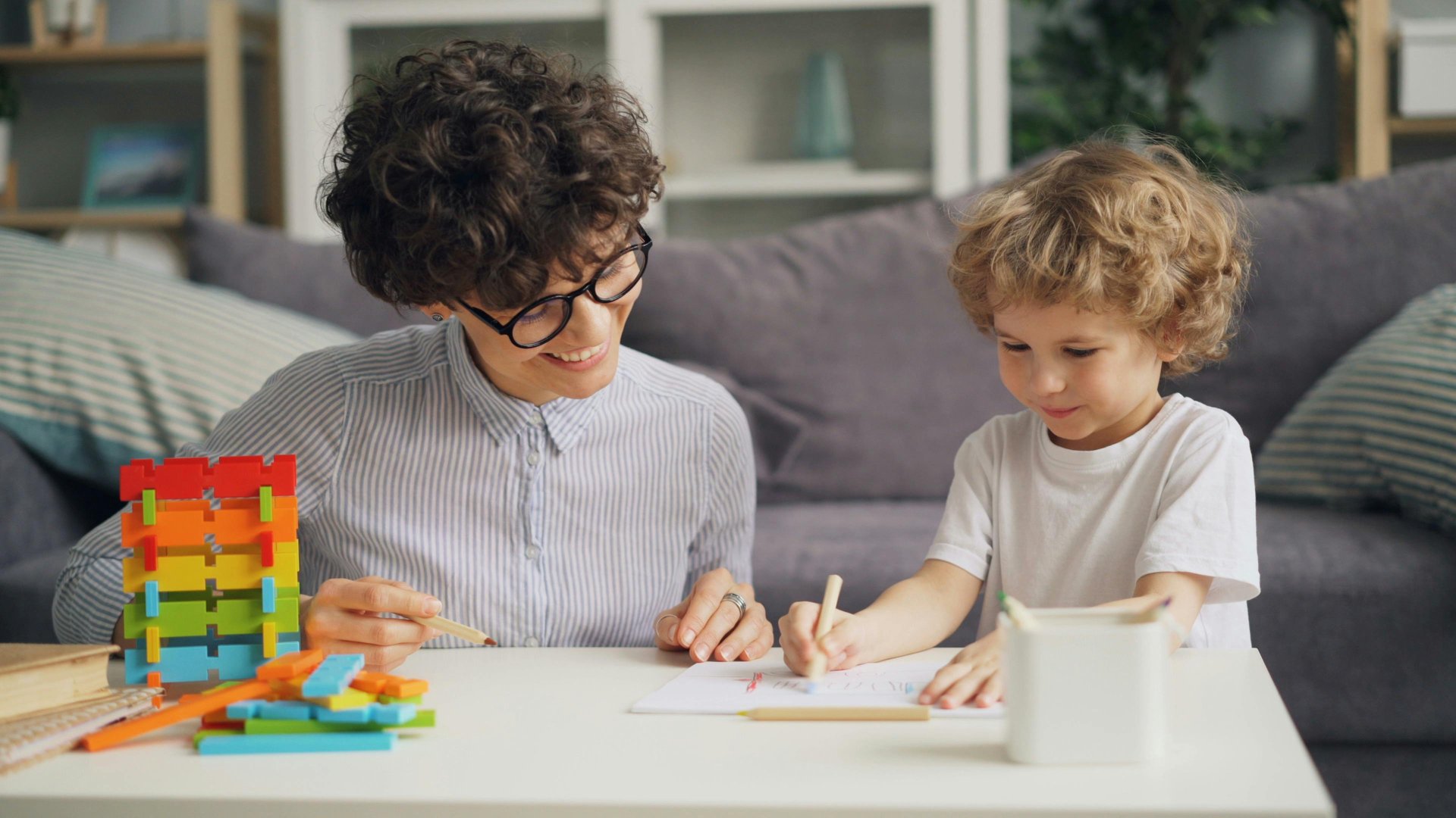 A clinician and young child working together at a table with rainbow blocks and drawing materials &mdash; representative of pediatric and behavioral therapy work