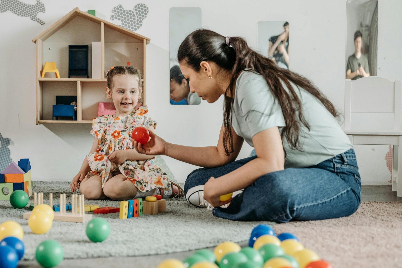 A clinician sitting on the floor of a pediatric clinic playroom, working with a young child using sensory and play-based materials